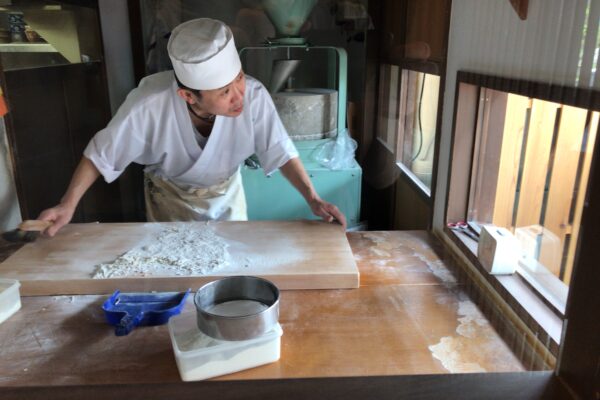 Soba-Meister bei der Arbeit. Im Hintergrund: Der Mahlstein.